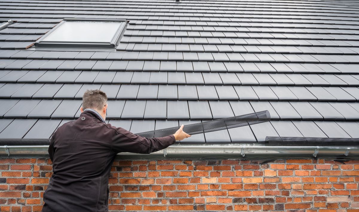 Installer fitting a gutter guard along a metal roof on a brick home