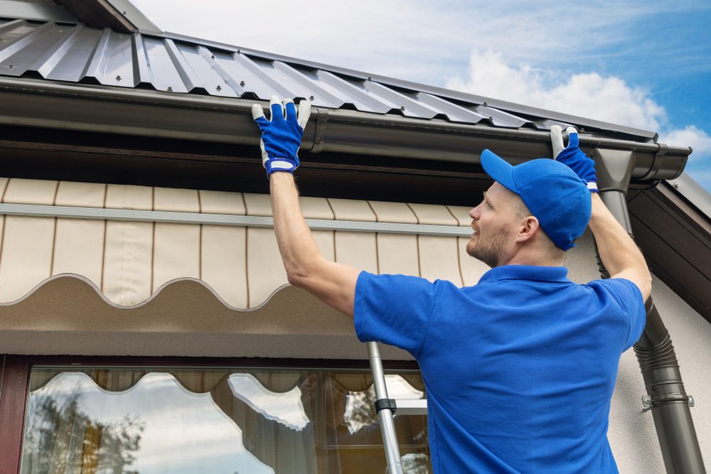 Technician reattaching a loose gutter section along a metal roof